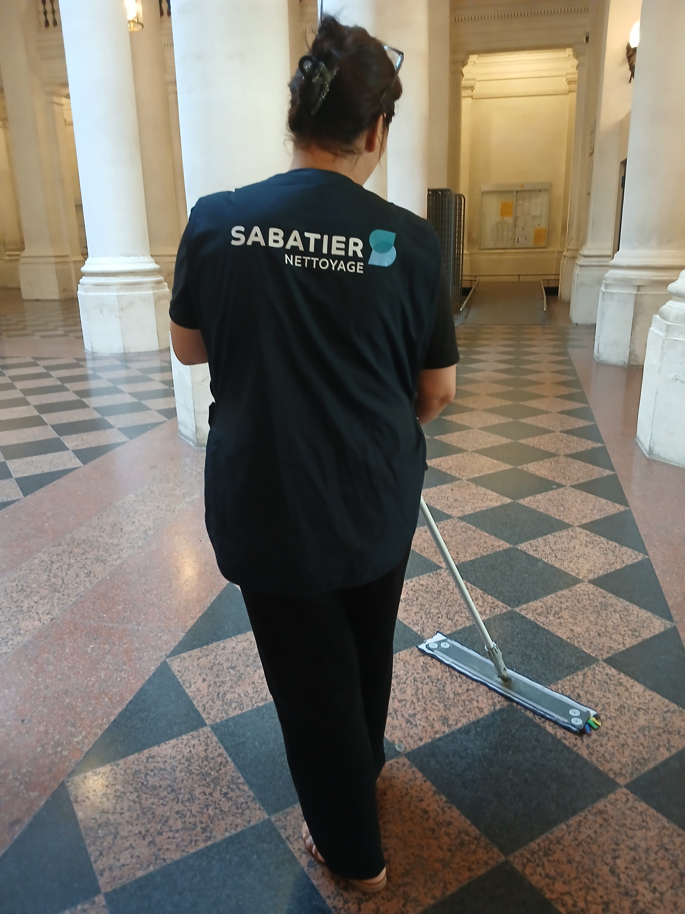 Agente de propreté réalisant l’entretien des sols dans un bâtiment historique avec colonnes.